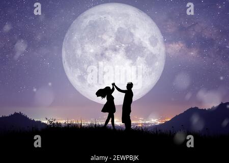 Silhouette at night landscape of couple or lover dancing and singing on the mountain with Milky way background over the full moon. Stock Photo