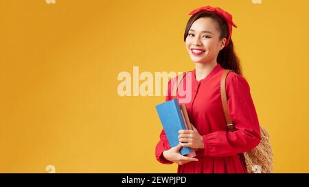 Pretty young girl in casual clothes with backpack posing isolated on yellow background. Education in high school university college concept. Hold book Stock Photo