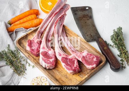 Organic pieces of mutton meat, Rack of lamb , raw with bone set, with ingredients carrot orange, herbs, and old butcher cleaver knife, on white stone Stock Photo