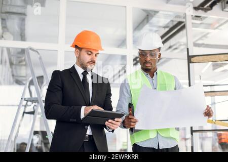 Caucasian and african men architects and builders in helmets working with blueprint Stock Photo