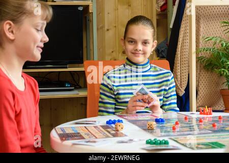 Children in a good mood are playing a board game, one of the girls looked into the frame Stock Photo