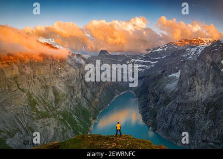 Man standing on rocks looking at clouds at sunset over lake Limmernsee, aerial view, Canton of Glarus, Switzerland, Europe Stock Photo