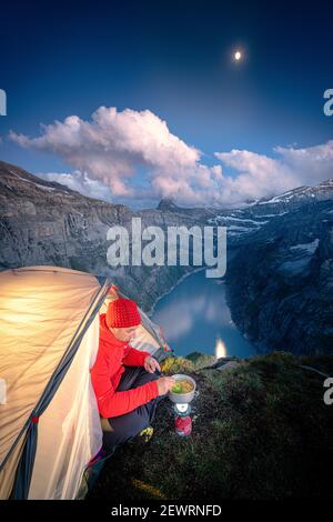 Hiker man cooking while camping in a tent above lake Limmernsee, Canton of Glarus, Switzerland, Europe Stock Photo