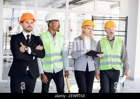Multiethnic four male and female architects and engineers in hardhats inspecting unfinished office building Stock Photo