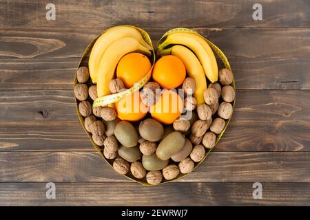 Top view of assorted fruit and dried fruits forming a heart on a dark wood background. Healthy eating and wellness concept. Space for text. Stock Photo