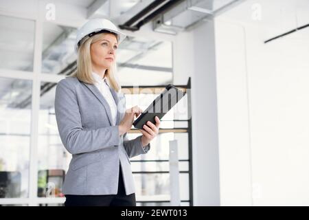Focused woman in formal wear and hardhat using tablet at work Stock Photo