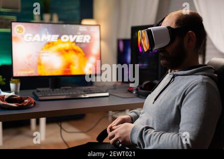 Defeated gamer man losing video game tournament playing with virtual reality headset. Competitive player using joystick for online competition late at night in gaming room Stock Photo