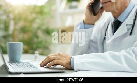 Doctor talking on mobile phone and using laptop at work Stock Photo