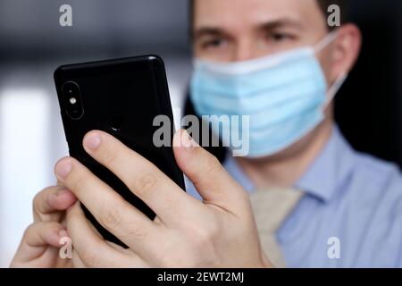 Smartphone in male hands close up, man in medical face mask and office clothes using mobile phone. Communication during coronavirus pandemic Stock Photo