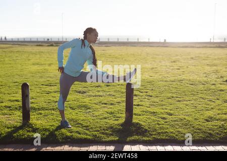 African american woman concentrating, wearing sports clothes exercising in a park stretching Stock Photo