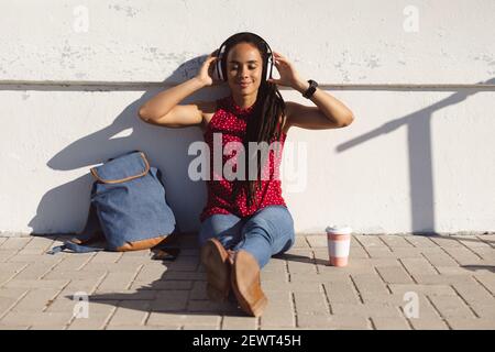 Happy african american woman smiling with eyes closed, sitting on pavement and listening to music Stock Photo