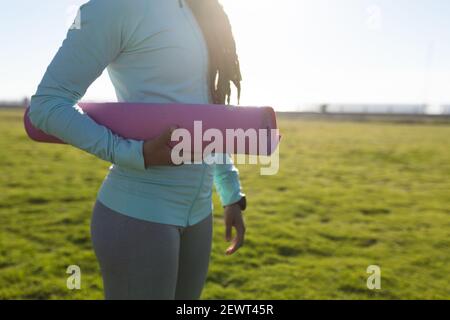 Midsection of african american woman exercising in a park carrying a yoga mat Stock Photo