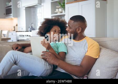African american girl sitting on couch using digital tablet with her father Stock Photo