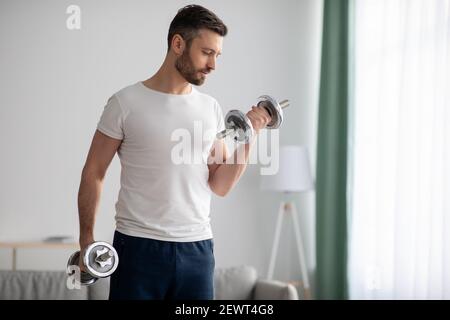 Closeup of handsome bearded man doing dumbbell workout at home Stock Photo