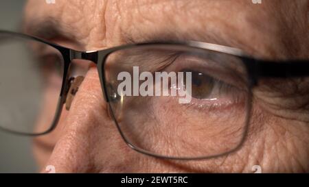 Close-up View of a Focused Mature Man Wearing Computer Glasses to Reduce Eye Strain, Reading the Internet until late Stock Photo