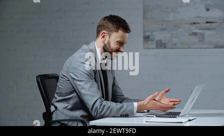 displeased young businessman gesturing while looking at laptop Stock Photo