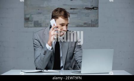 businessman in suit talking on smartphone and using laptop in office Stock Photo