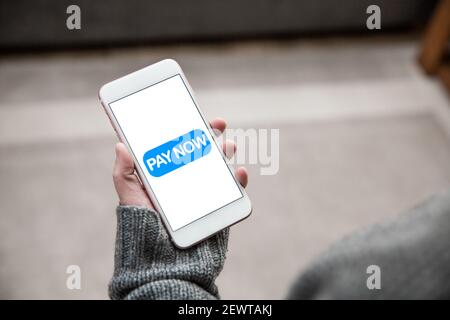 A girl holding a mobile phone and tapping a Pay Now icon to make a payment transaction for online shopping Stock Photo