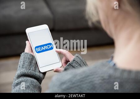 A woman tapping a search icon on her mobile phone whilst looking for online content information Stock Photo