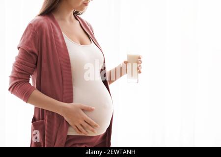 Unrecognizable Pregnant Woman With Glass Of Milk In Hands Standing Near Window Stock Photo