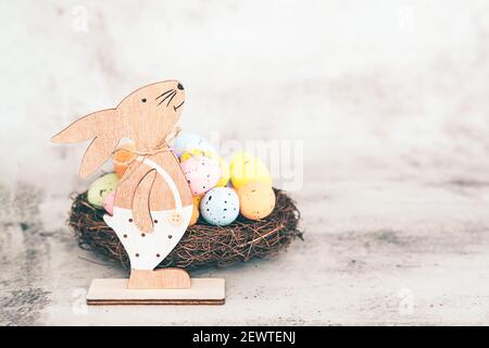 Wooden bunny and nest with easter eggs on light gray background Stock Photo