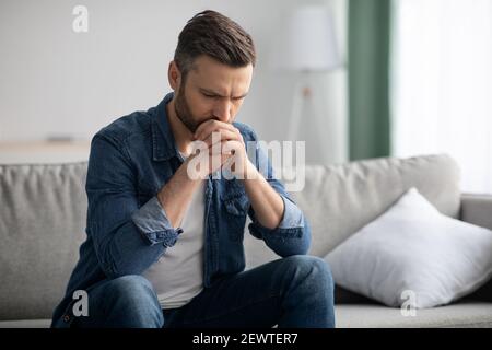 Upset bearded man sitting on sofa in living room Stock Photo