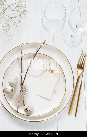 Easter table setting with willow twigs, quail eggs and tag. Golden cutlery and golden rim plates. Stock Photo