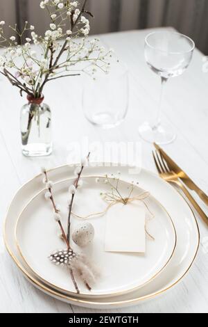 Easter table setting with willow twigs, quail eggs and tag. Golden cutlery and golden rim plates. Stock Photo