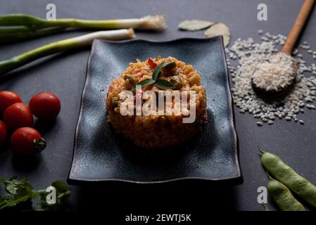 italian vegan spring risotto on black dish with asparagus on dark background. healthy and fresh springtime vegetables like carrots, cherry tomatoes an Stock Photo