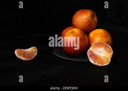 Whole and halved red oranges on black surface.
