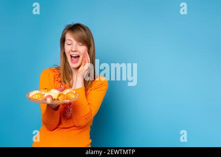 Excited young woman 20s in casual orange shirt hold makizushi sushi roll served on glass crystal plate . Traditional japanese food isolated on blue Stock Photo