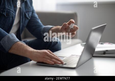 Closeup of male hand using disinfectant spray for cleaning laptop Stock Photo