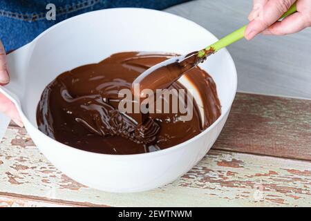 Confectioner tempering chocolate with a spatula in a white bowl. Stock Photo