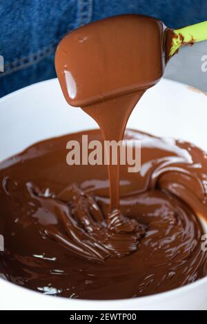 Closeup of a spatula with tempered chocolate falling into a white bowl. Stock Photo