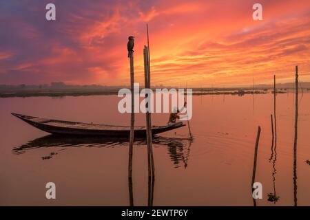 Boatman rows his fishing boat close to the river bank at sunset with scenic rural landscape at West Bengal India Stock Photo