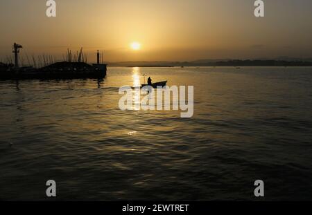 Small boat with lone person heading out to fish from the marina in Santander Cantabria Spain Early morning with low sun Stock Photo