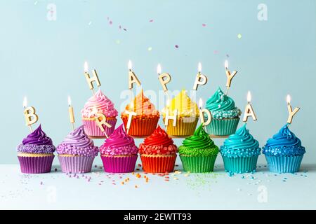 Rainbow colored cupcakes with birthday candles spelling happy birthday Stock Photo