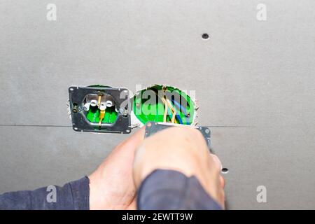The electrician plugs electrical outlets into the socket boxes in the drywall. Repair and home improvement. Stock Photo