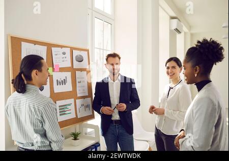 Cheerful diverse office workers discuss financial risks and analyze charts and diagrams together. Stock Photo