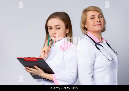 Serious surgeon team of doctors having a meeting at hospital. Thoughtfully pretty female practitioners with clipboard looking at camera on white Stock Photo