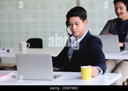 Asian businessman in headphones looking at laptop, watching good webinar, consulting client, distance learning languages, making notes, happy man Stock Photo