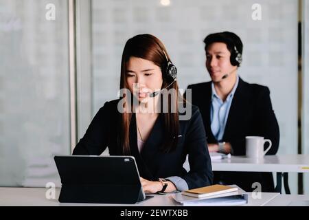 Young asian woman working in call centre, surrounded by colleagues. Stock Photo