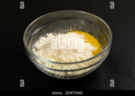 Grainy cottage cheese, egg, flour in a glass bowl on a black table close-up Stock Photo