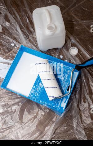 Tools for priming plastered surfaces for further painting.Paint roller in a blue tray with white paint on dirty floor background. Renovation, painting Stock Photo