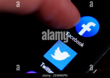 Madrid, Spain- March 3, 2021: Finger pressing Facebook icon on black mobile phone screen. Twitter icon in the background. Stock Photo