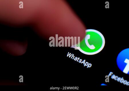 Madrid, Spain- March 3, 2021: Finger pressing Whatsapp icon on black mobile phone screen. Facebook icon in the background. Stock Photo