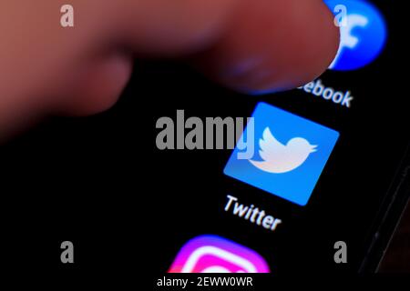 Madrid, Spain- March 3, 2021: Finger pressing Twitter icon on black mobile phone screen. Instagram and Facebook icon in the background. Stock Photo