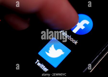 Madrid, Spain- March 3, 2021: Finger pressing Facebook icon on black mobile phone screen. Twitter icon in the background. Stock Photo