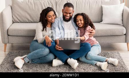 Happy black family using laptop sitting on the floor Stock Photo
