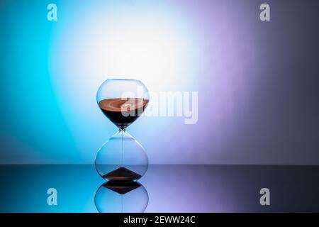 Hourglass standing on mirror surface in neon light Stock Photo